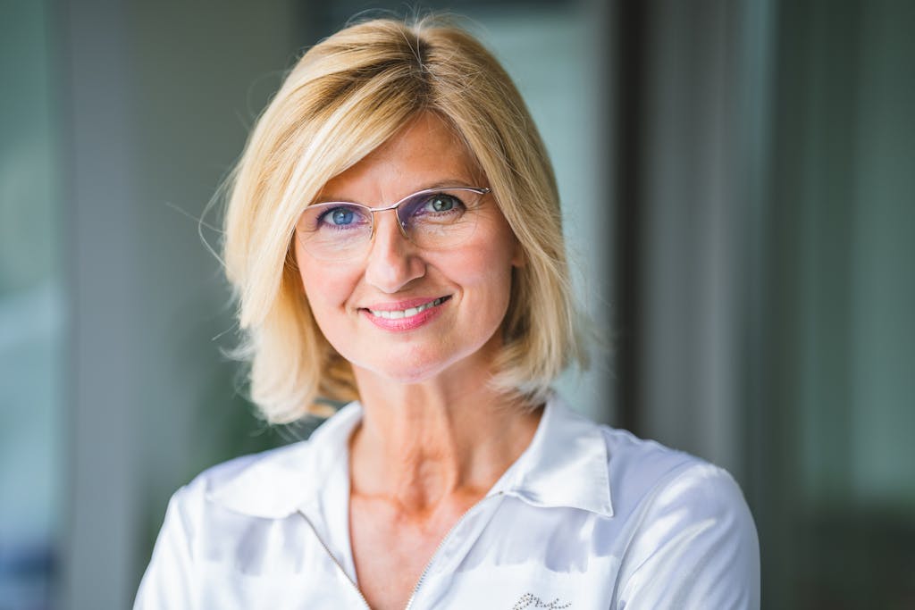 Close-up of a smiling blonde woman wearing eyeglasses indoors.