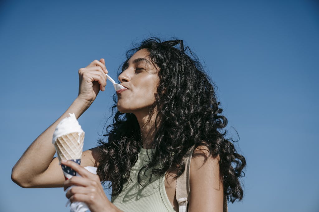 Woman savors creamy ice cream cone outdoors on a sunny day, embracing summer vibes.